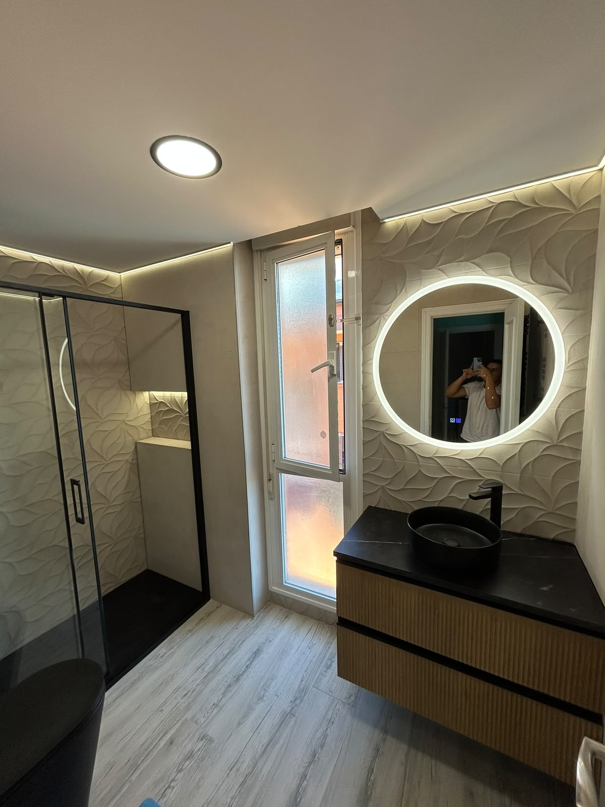 Baño reformado con ducha, mampara negra, iluminación integrada y mueble de lavabo
